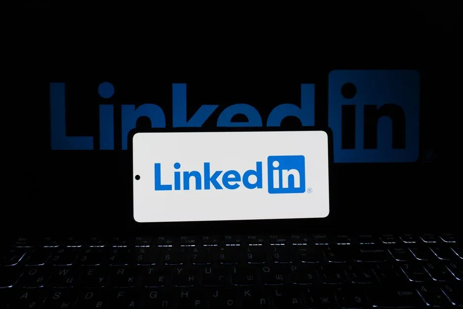 Smartphone showing LinkedIn logo with keyboard and large background logo, business theme.